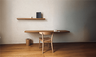 Minimalist workspace featuring a sleek wooden table and chair, with a shelf displaying books and a small decorative item. The room exudes simplicity and tranquility.